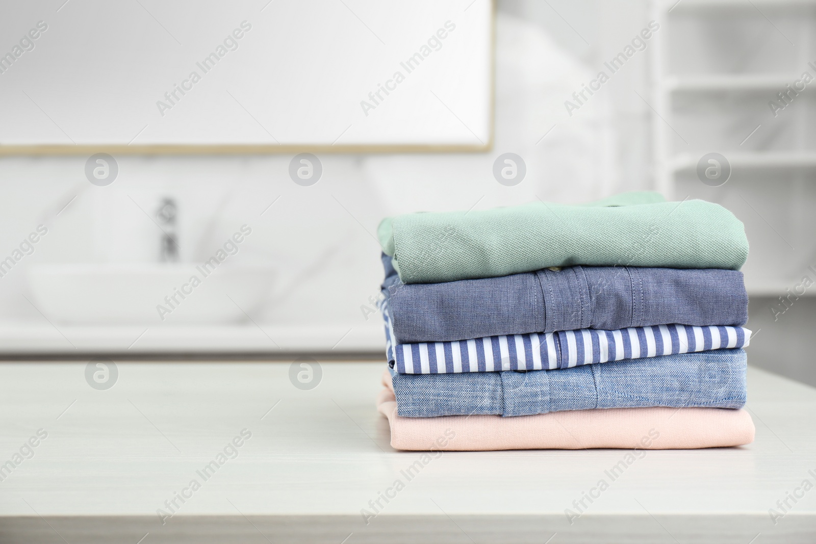 Photo of Fresh laundry on white wooden table in bathroom. Space for text