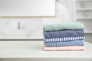 Fresh laundry on white wooden table in bathroom. Space for text