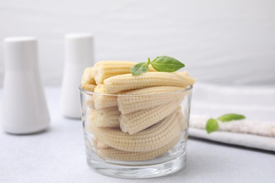 Photo of Canned baby corns with basil on white table, closeup