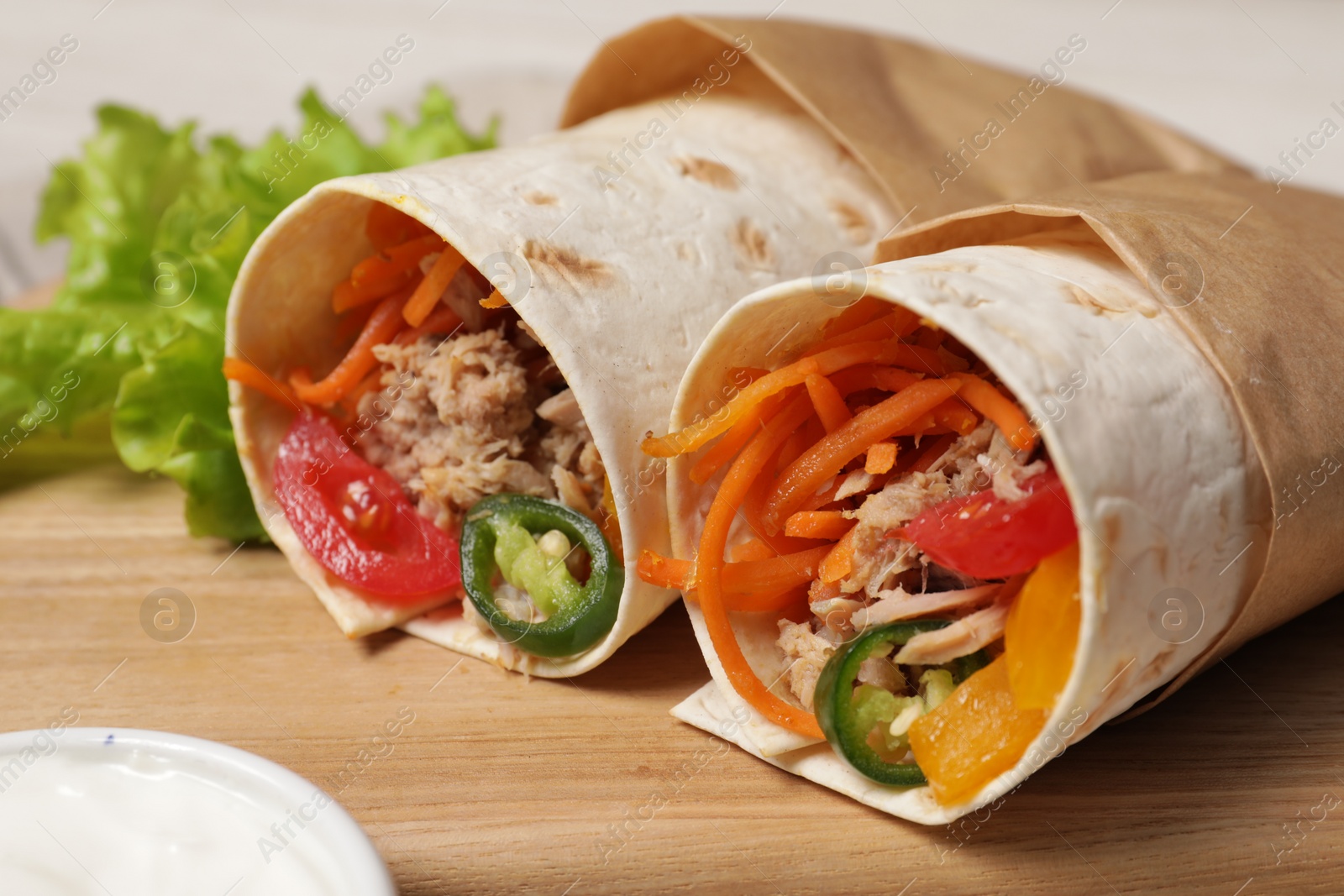 Photo of Delicious tortilla wraps with tuna on wooden board, closeup