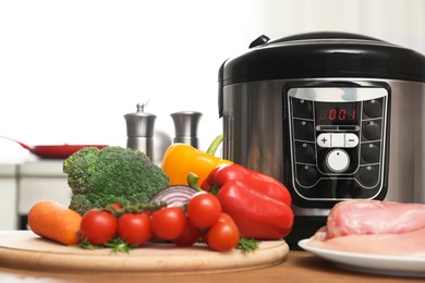 Photo of Modern multi cooker and ingredients on wooden table in kitchen. Space for text