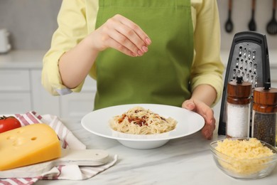 Photo of Woman pouring grated cheese onto delicious pasta at white marble table in kitchen, closeup