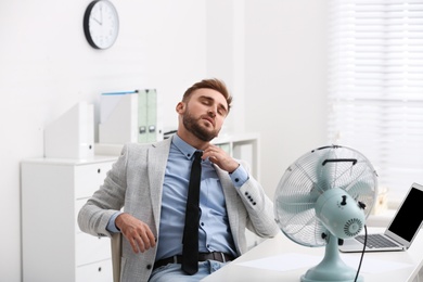 Man suffering from heat in front of fan at workplace