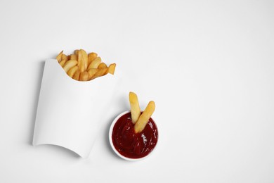 Photo of Paper cup with French fries and ketchup on white table, flat lay. Space for text