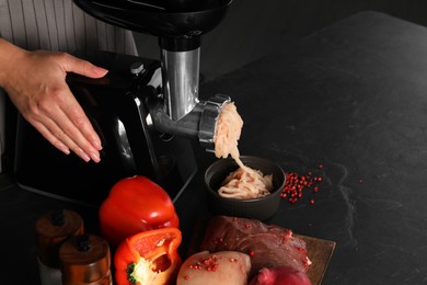 Photo of Woman making chicken mince with electric meat grinder at black table, closeup. Space for text