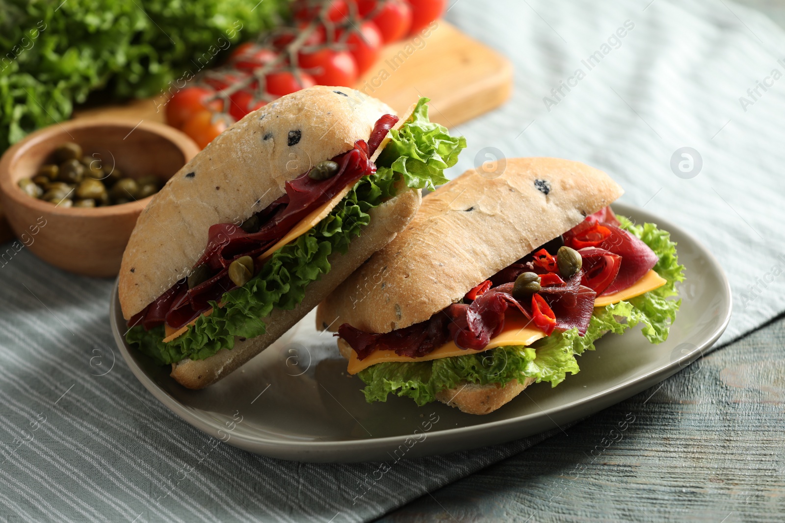 Photo of Delicious sandwiches with bresaola, cheese and lettuce on light blue wooden table