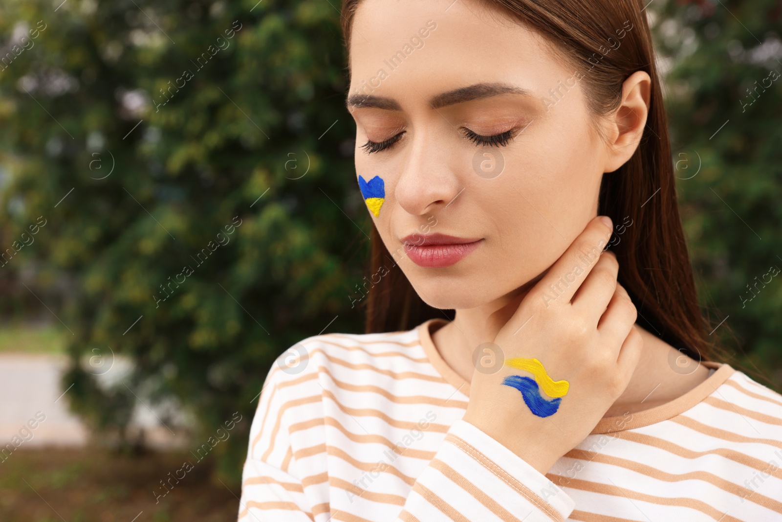 Photo of Young woman with drawings of Ukrainian flag outdoors, closeup. Space for text