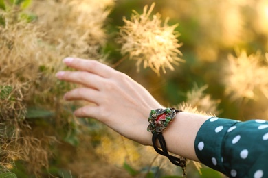 Young woman wearing beautiful metal bracelet with carnelian and gemstones outdoors, closeup