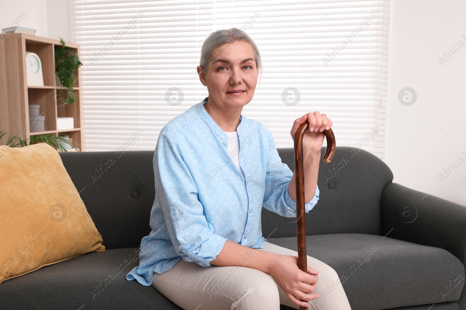 Photo of Senior woman with walking cane sitting on sofa at home. Space for text