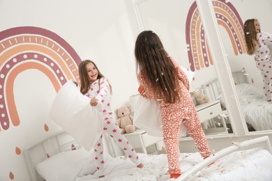 Cute little girls in pajamas having pillow fight on bed at home. Happy childhood