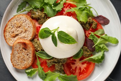 Photo of Delicious burrata salad with tomatoes, arugula and pesto sauce on black table, top view