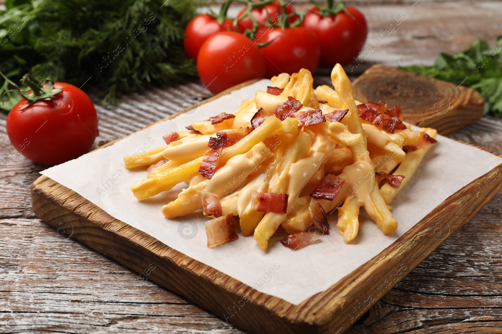 Photo of Delicious French fries with bacon, cheese sauce, tomatoes and dill on wooden table, closeup