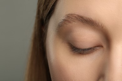 Woman with beautiful natural eyelashes on grey background, closeup