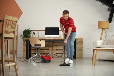 Photo of Young man using vacuum cleaner at home