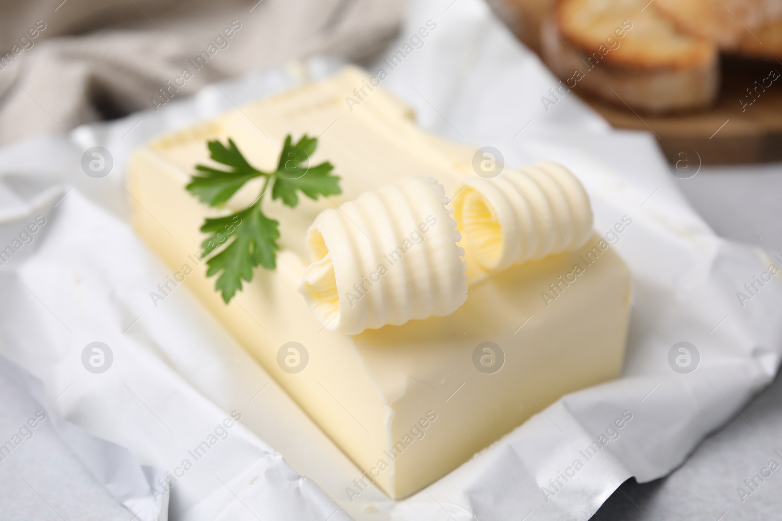 Photo of Tasty butter with curl and parsley on light grey table, closeup