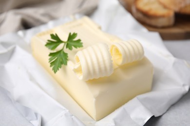 Photo of Tasty butter with curl and parsley on light grey table, closeup