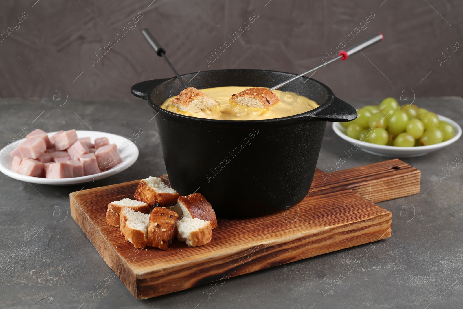 Photo of Fondue pot with tasty melted cheese, forks and different snacks on grey table