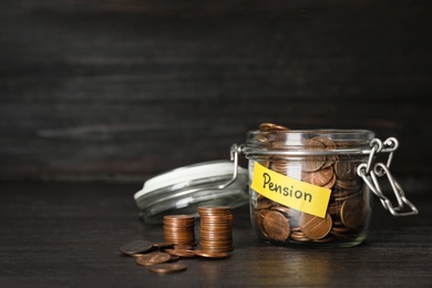 Photo of Coins in glass jar with label "PENSION" on dark table. Space for text