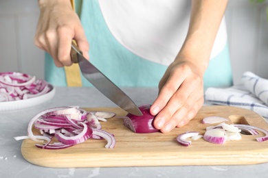 Photo of Woman cutting fresh red onion on wooden board at table, closeup