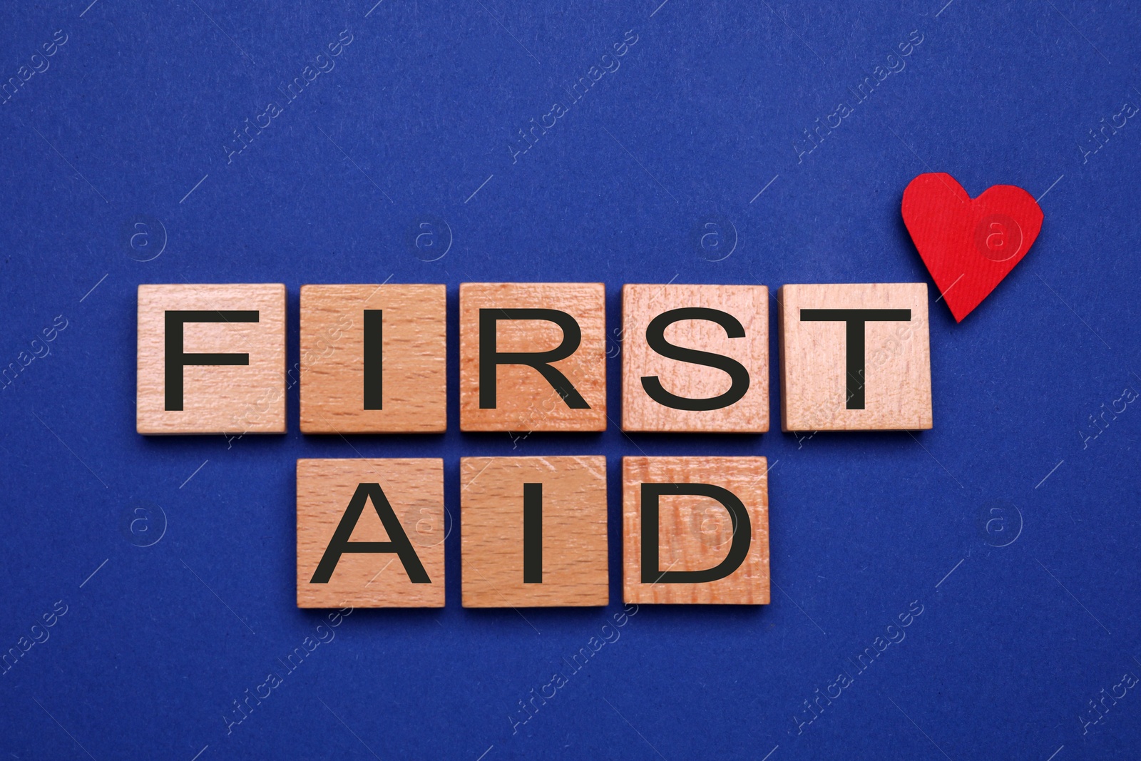 Photo of Words First Aid made of wooden cubes and paper heart on blue background, flat lay