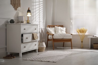 Stylish room interior with white chest of drawers and comfortable armchair