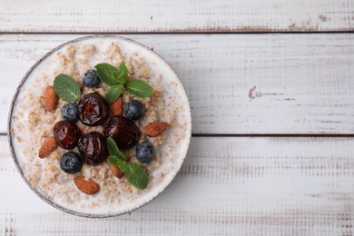 Tasty wheat porridge with milk, dates, blueberries and almonds in bowl on light wooden table, top view. Space for text