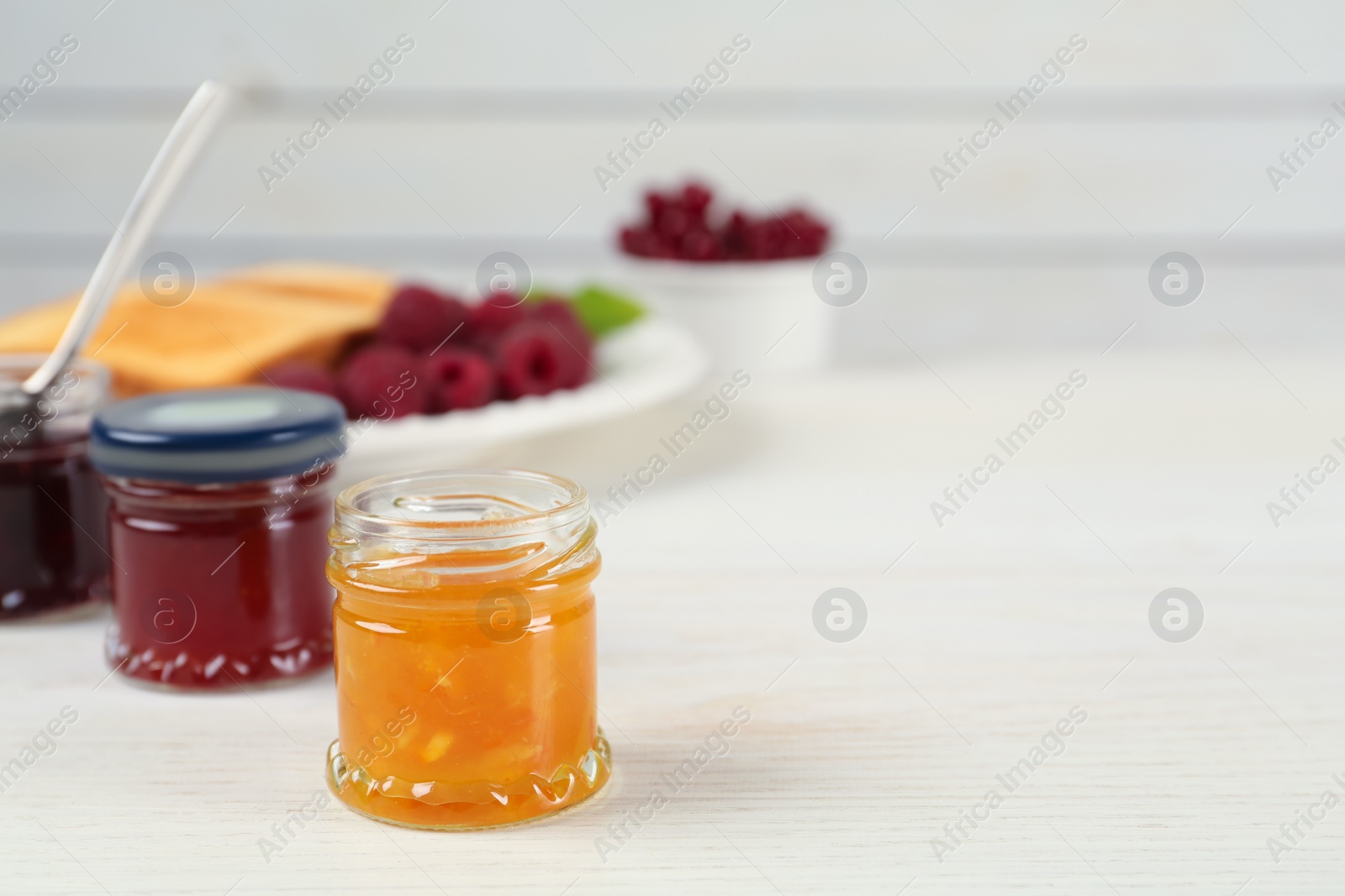 Photo of Jars with different sweet jams on white wooden table. Space for text