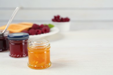 Jars with different sweet jams on white wooden table. Space for text