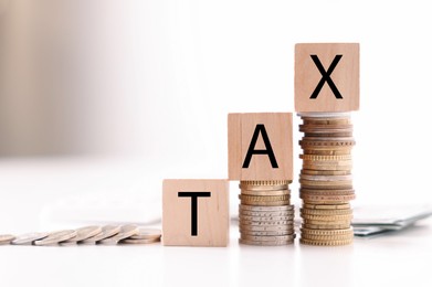 Photo of Word Tax made of wooden cubes and coins on white table