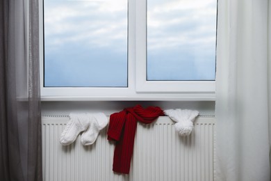 Heating radiator with hat, socks and scarf near window indoors
