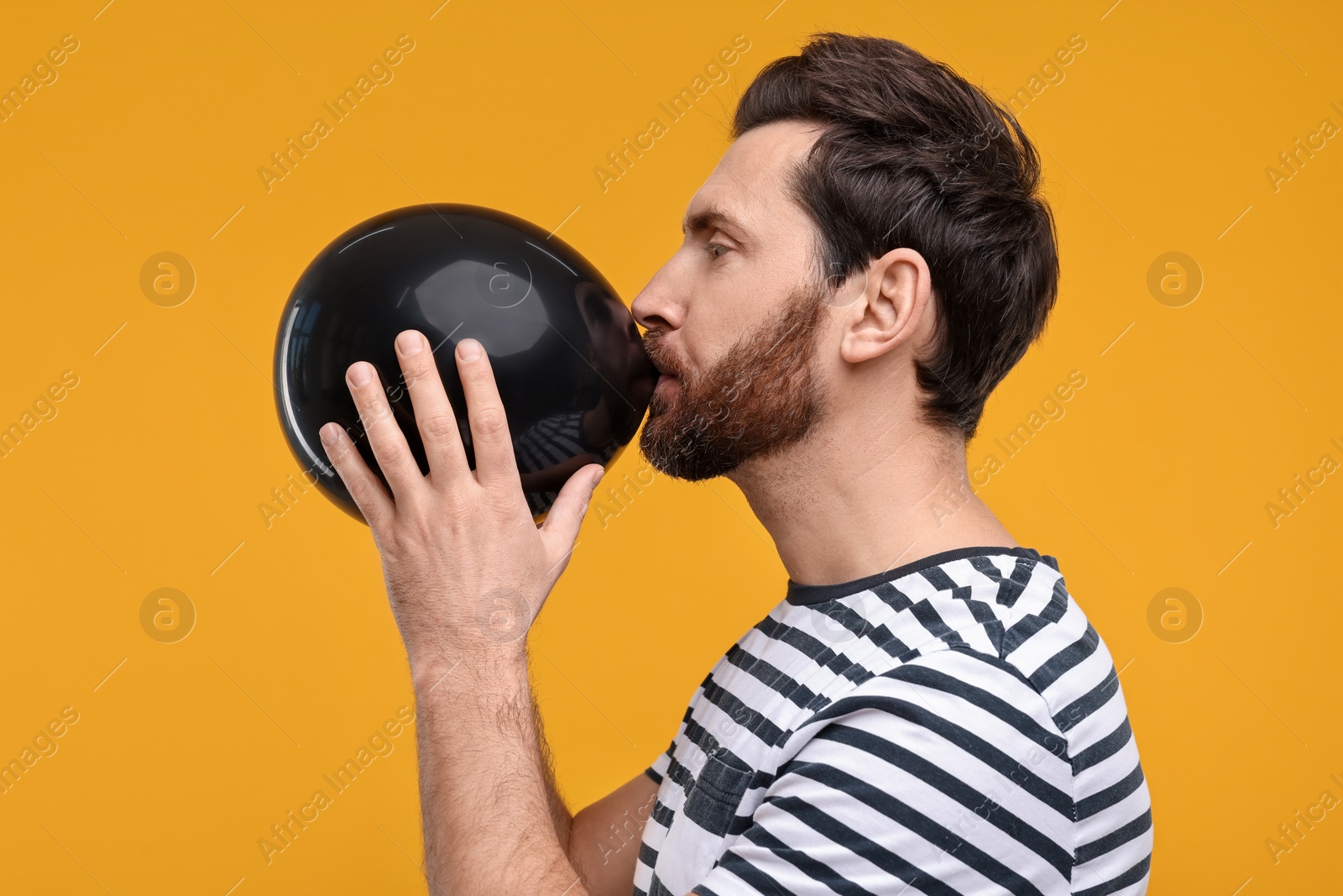 Photo of Man inflating black balloon on yellow background