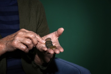 Poor senior woman with coins on color background, closeup. Space for text