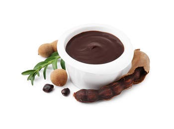 Photo of Bowl of tasty tamarind sauce, leaves and fresh pods isolated on white