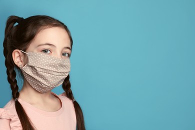 Photo of Girl wearing protective mask on light blue background, space for text. Child's safety from virus