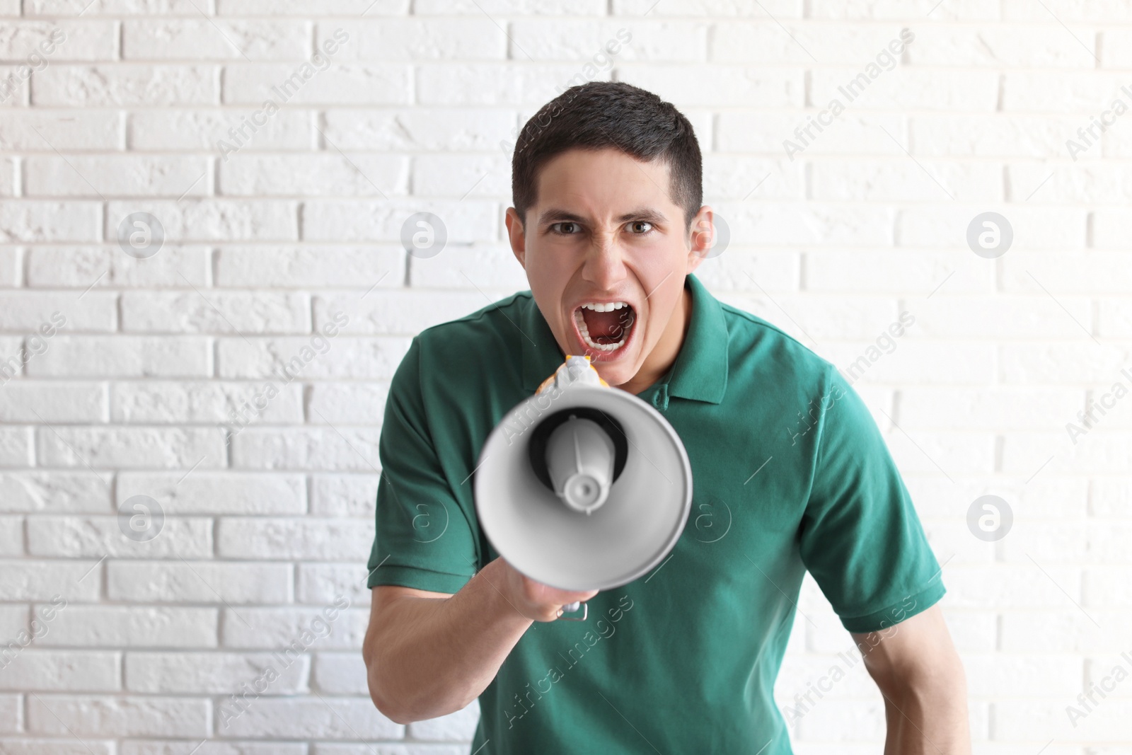 Photo of Portrait of young man using megaphone near brick wall