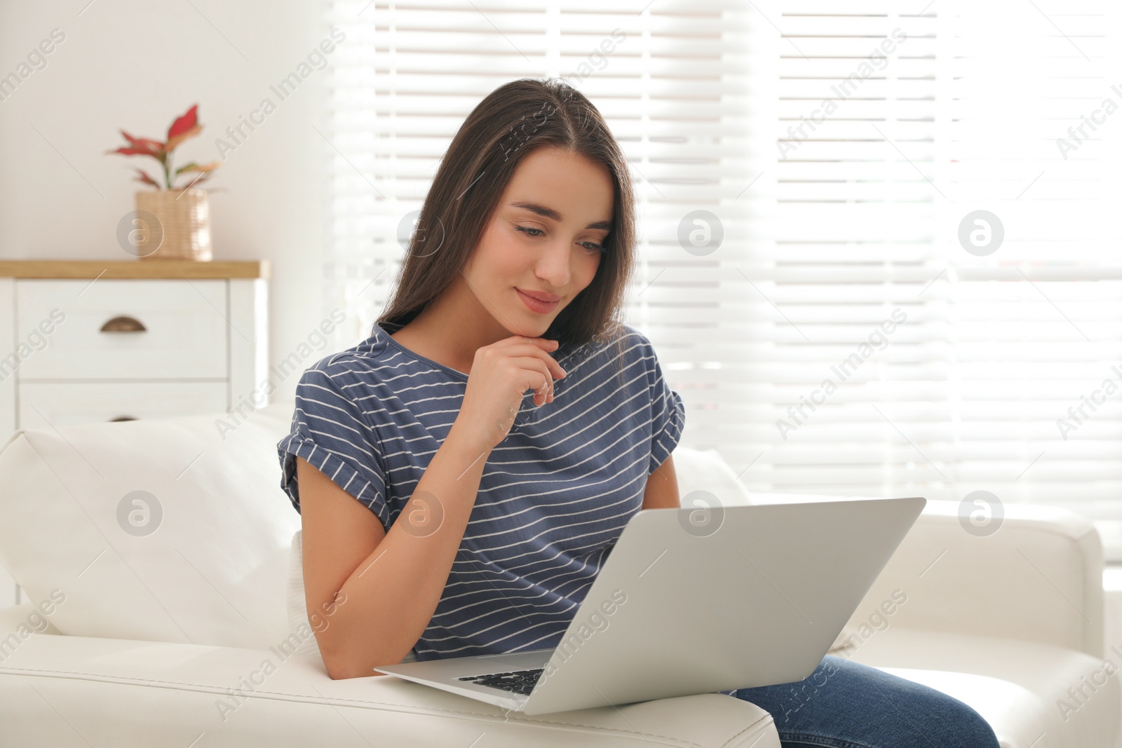 Photo of Young woman using laptop for search on sofa at home