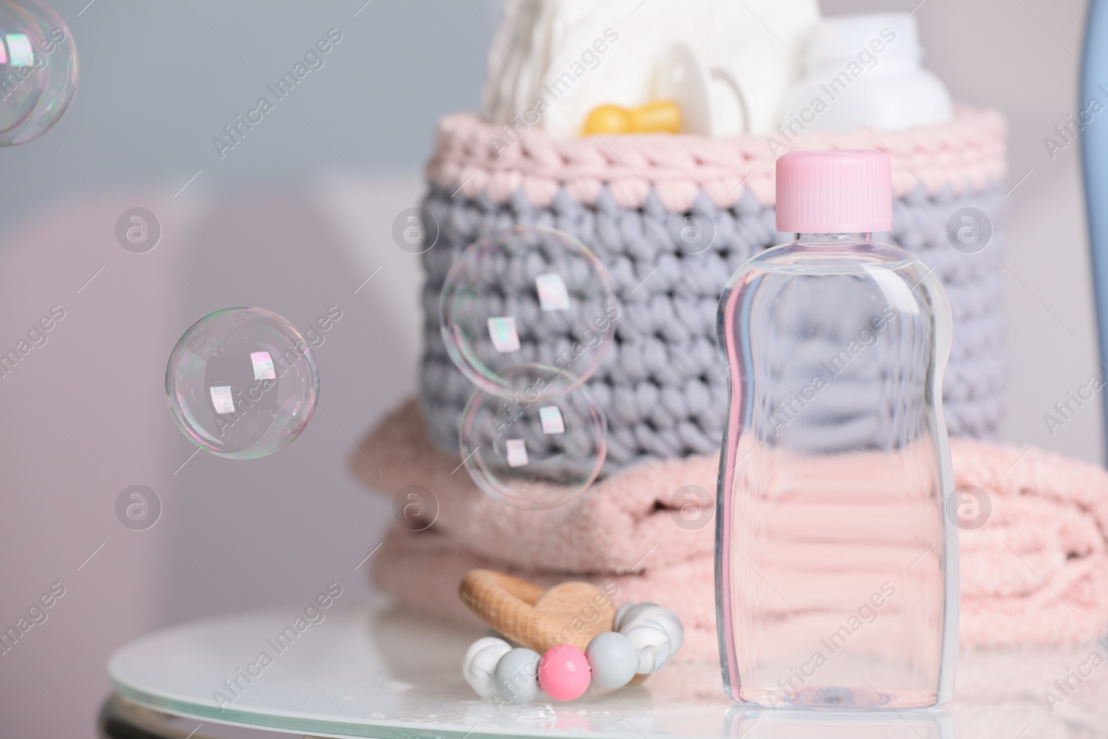 Photo of Bottle of baby cosmetic product, wooden toy and accessories on white table against color background. Space for text