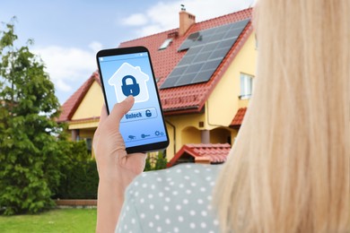 Image of Woman using home security system application on smartphone outdoors, closeup