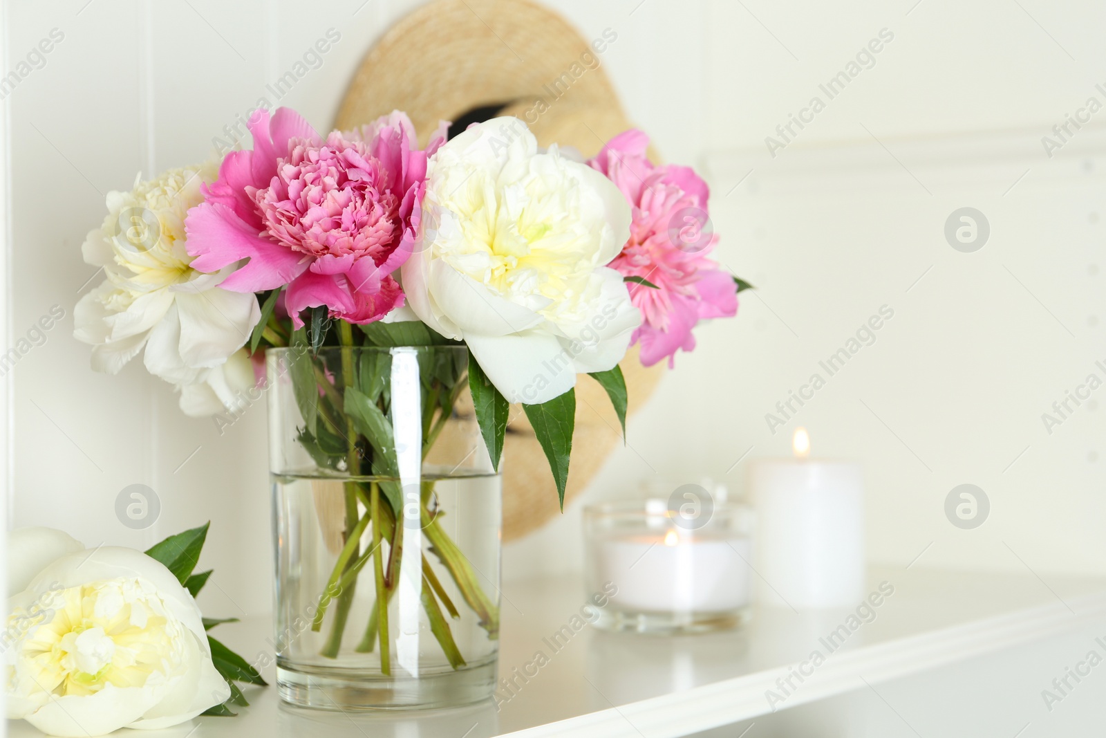 Photo of Bouquet of beautiful peonies in vase and candles on white table