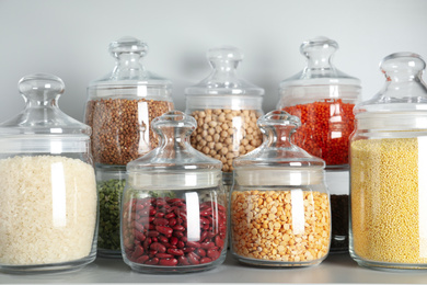 Photo of Glass jars with different types of groats and pasta on white shelf