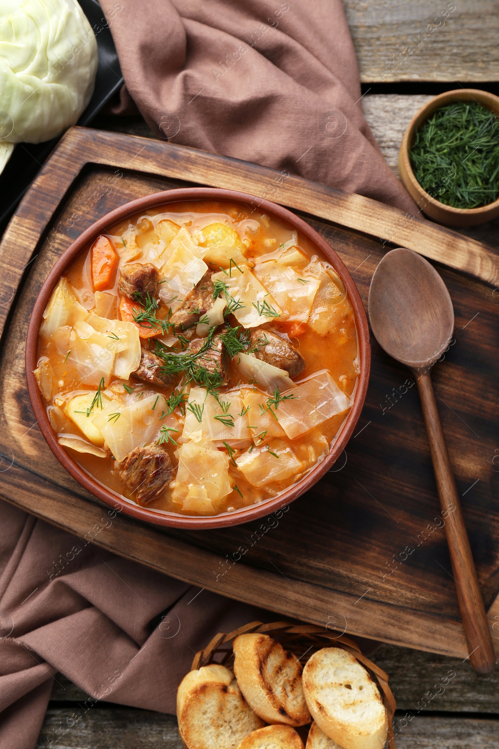 Photo of Tasty cabbage soup with meat, carrot and ingredients on wooden table, flat lay