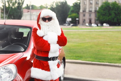 Authentic Santa Claus with sunglasses near car outdoors