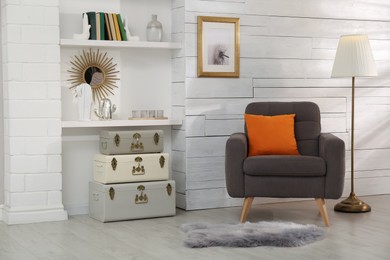Photo of Stylish room interior with comfortable armchair and storage trunks near white wall