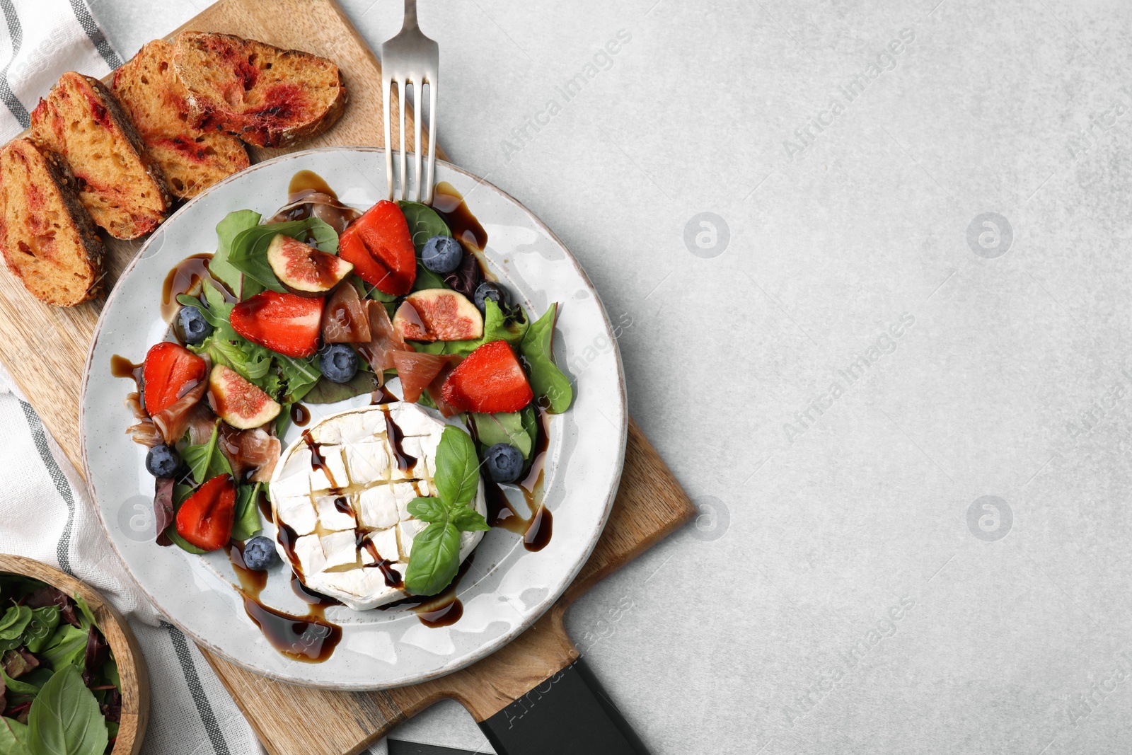 Photo of Delicious salad with brie cheese, prosciutto, berries and balsamic vinegar served on light grey table, flat lay. Space for text