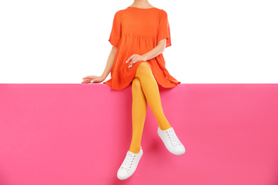 Woman wearing yellow tights and stylish shoes sitting on color background, closeup