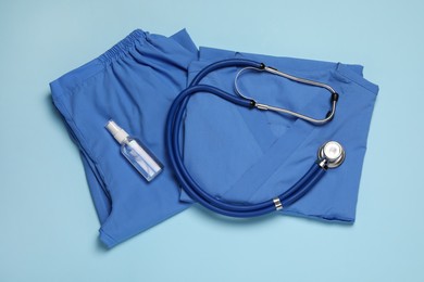 Photo of Medical uniform, stethoscope and antiseptic on light blue background, flat lay