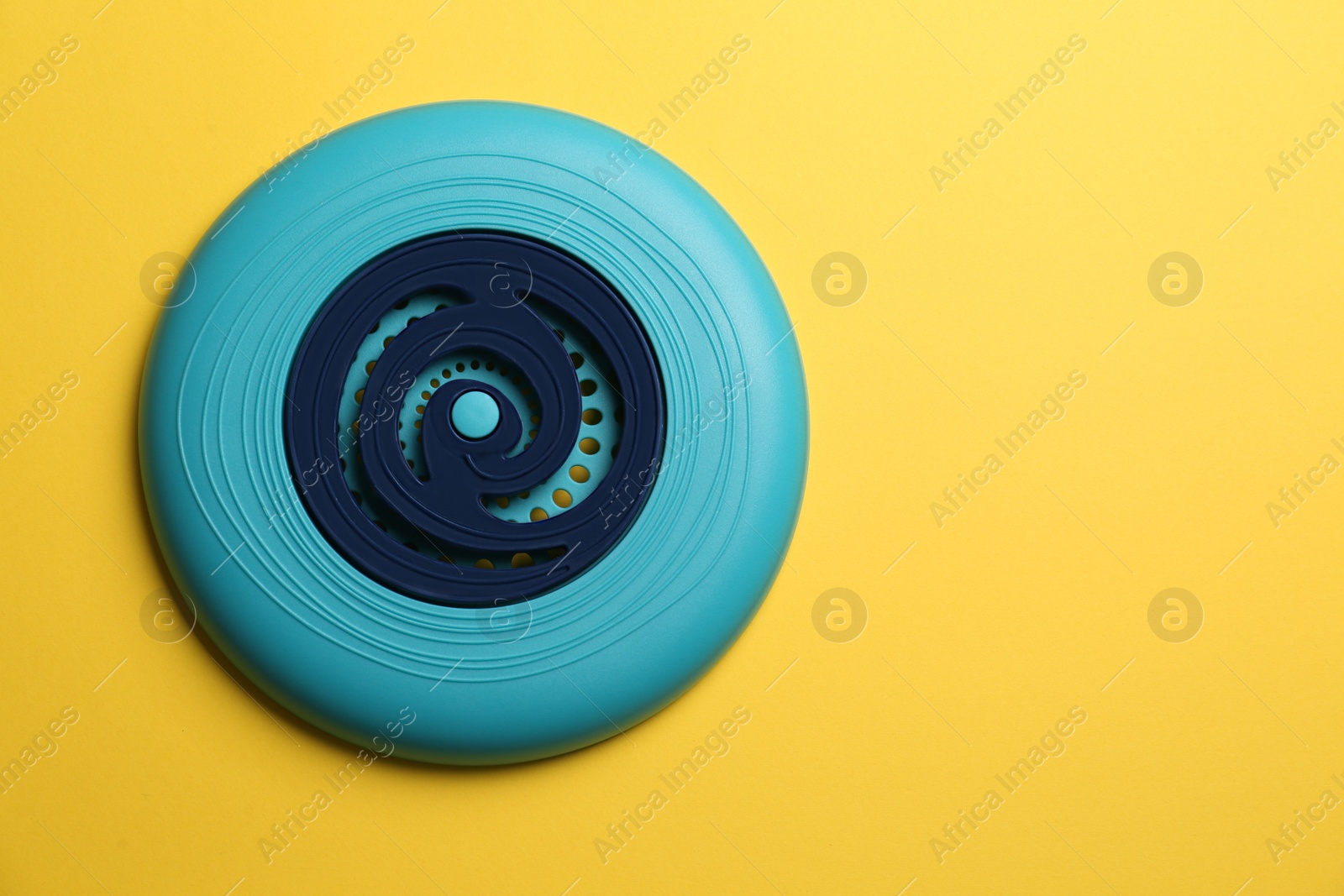 Photo of Blue plastic frisbee disk on yellow background, top view. Space for text