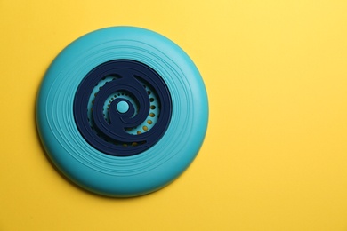 Blue plastic frisbee disk on yellow background, top view. Space for text