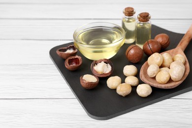 Delicious organic Macadamia nuts and cosmetic oil on white wooden table. Space for text