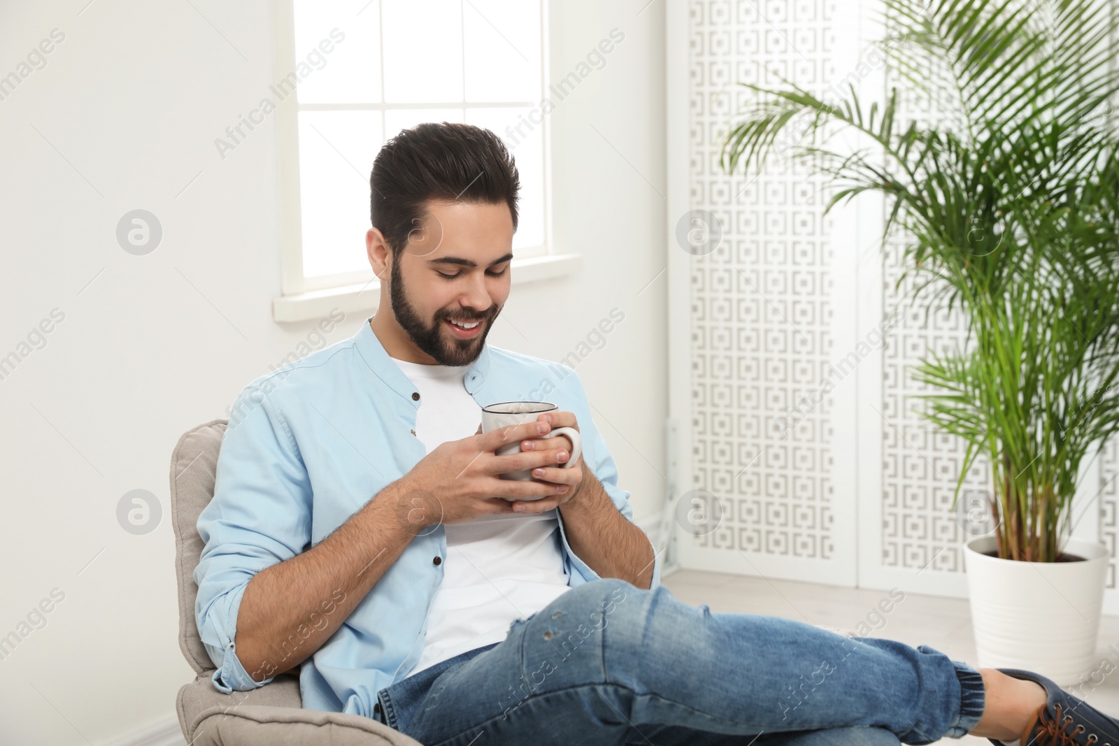 Photo of Young man with cup of drink relaxing at home